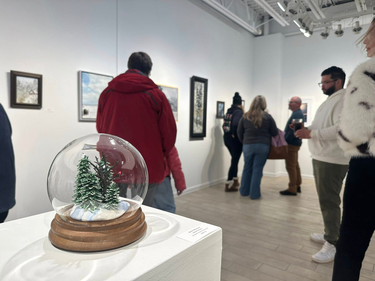 People visiting an art gallery with a snow globe on display.