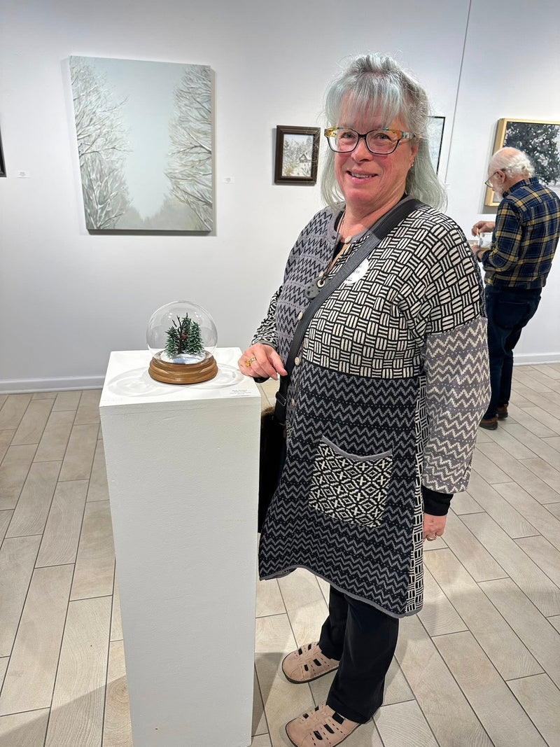 Woman standing in an art gallery with a small sculpture on a pedestal.