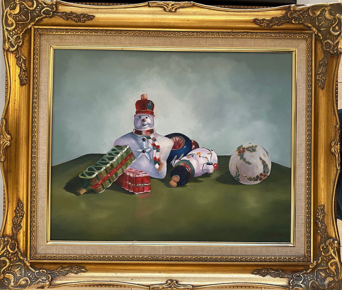 Framed artwork of ceramic figures on a table with a gold frame.