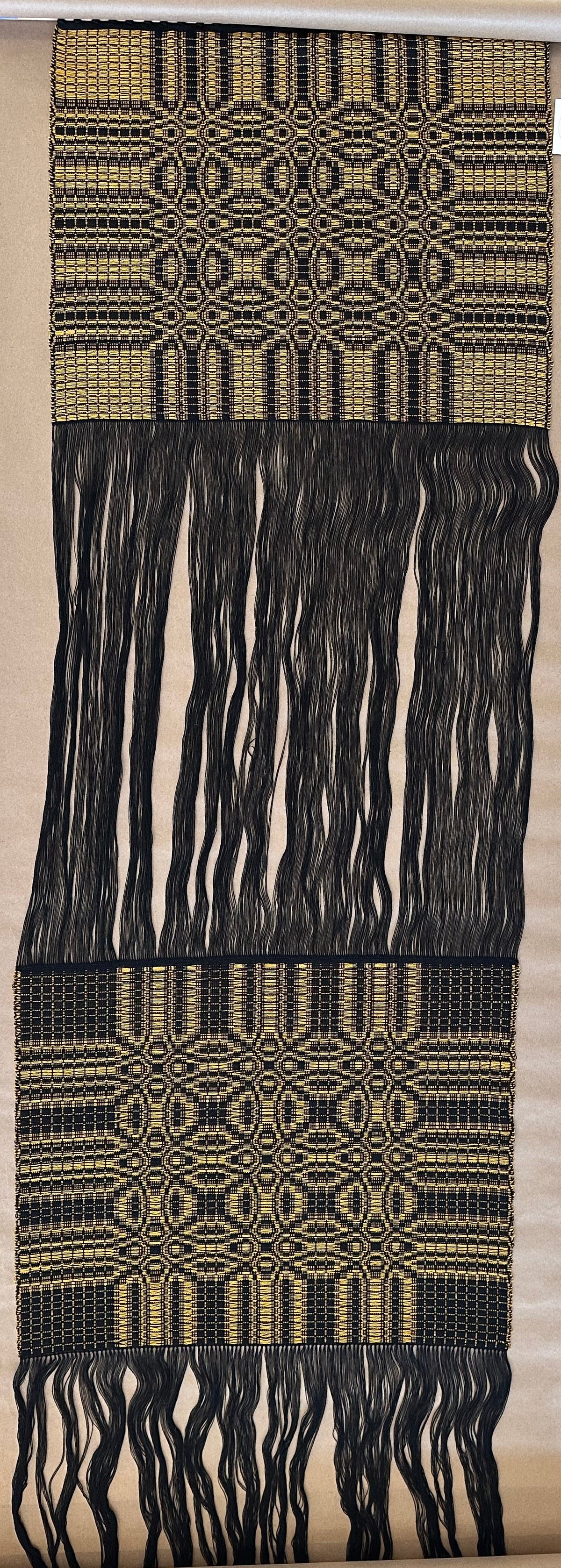 Textile sample with black and gold patterns on a wooden floor