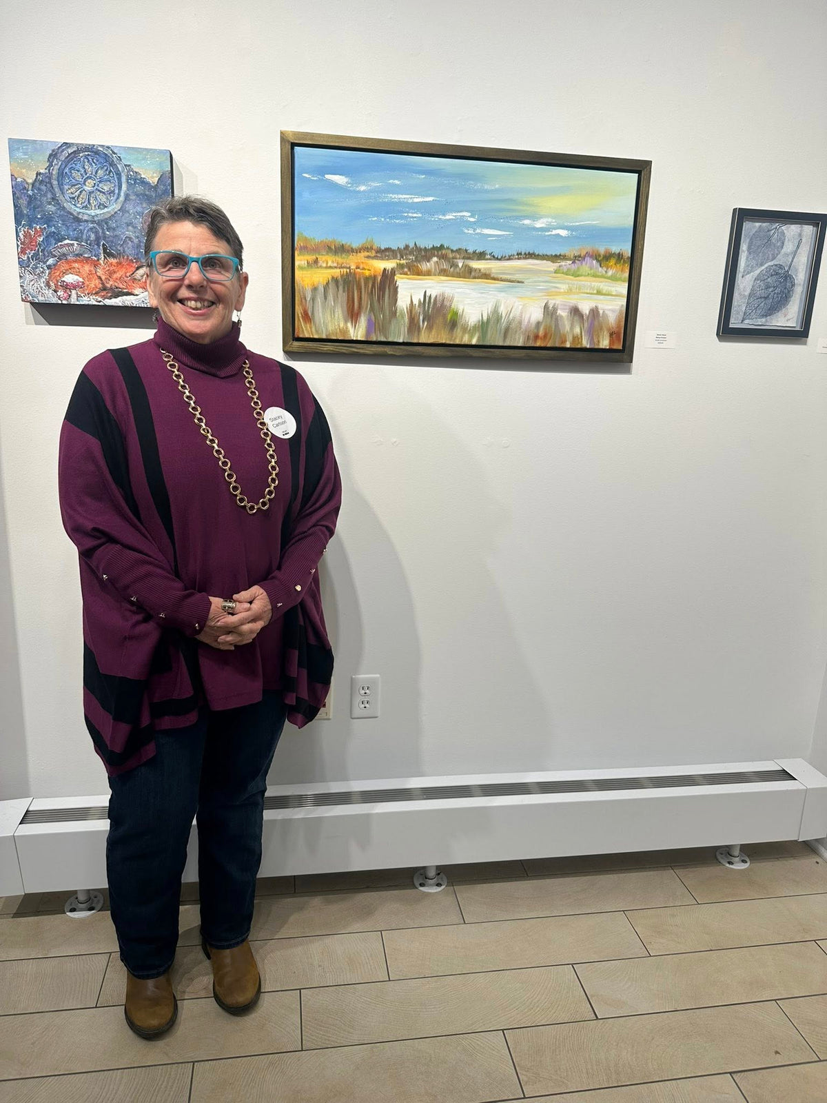 Person standing in front of wall with framed artworks in an art gallery.